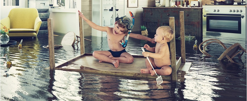 A képen egy vízzel elárasztott szoba látható, amelyben két kisgyermek játszik, a felfordított asztalt csónaknak használva.