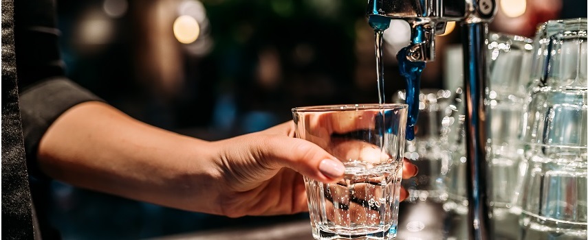 A képen egy kézben tartott pohár látható, amelybe vizet engednek. 