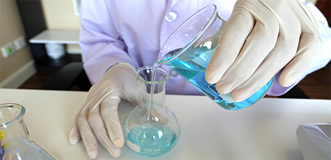 A képen laboratóriumban történő folyadékvizsgálathoz előkészület látható, folyadékminta kerül egy kisebb üvegbe.