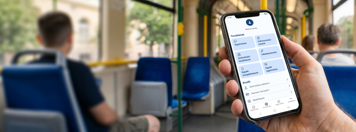 A képen egy mobiltelefont tartó ember keze látható, aki az applikációban éppen ügyintéz, miközben buszon utazik.