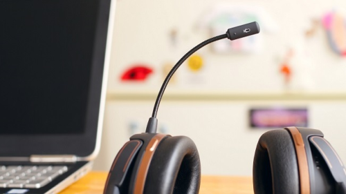A kép illusztráció, mely irodai környezetben készült, egy professzionális fejhallgató látható rajta mikrofonnal egy asztalon, egy monitor mellett.